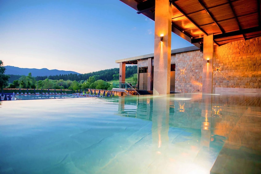 A swimming pool with a wooden deck, stone walls, and a view of mountains in the background. 3