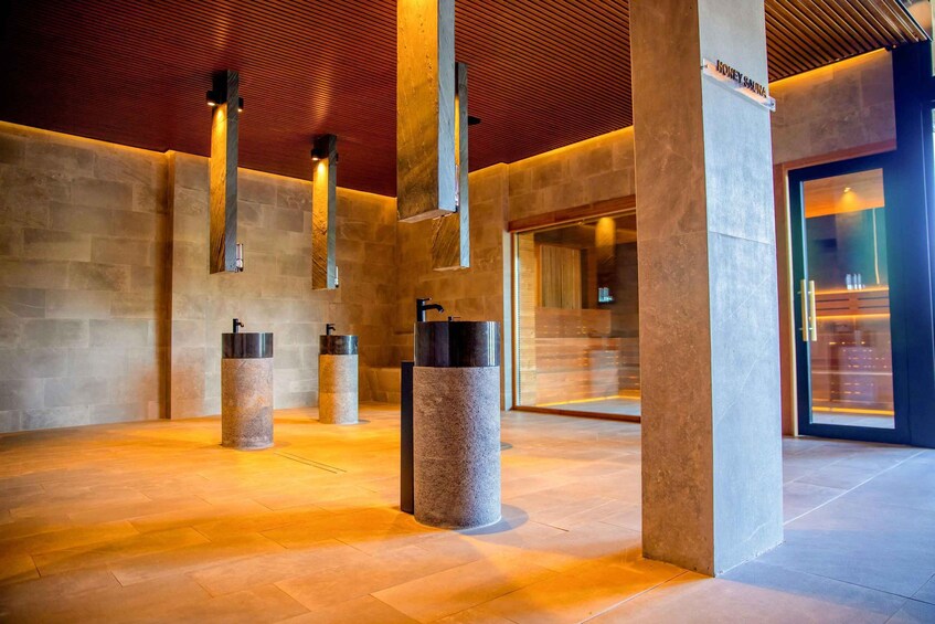 A modern interior with stone pillars, wooden slats on the ceiling, and a glass door labeled 'Honey Sauna'. 2
