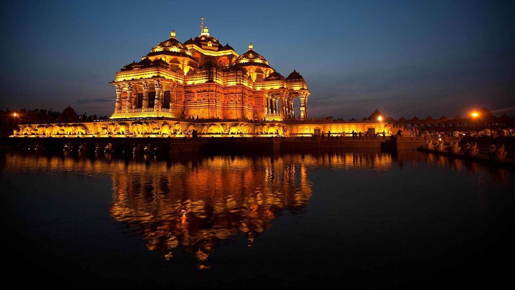 A brightly lit temple with intricate carvings, reflecting on the water in front of it. 4