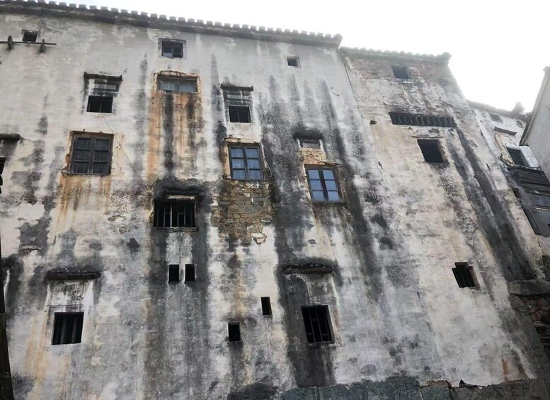 A weathered building with multiple windows, some of which are boarded up or broken. 4