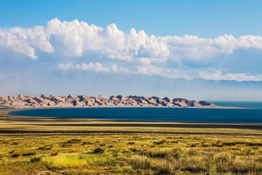 A vast landscape with rolling sand dunes, a body of water, and a clear sky. 3