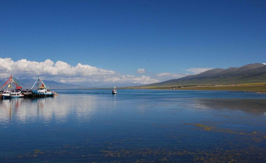 A calm lake with fishing boats, a small boat, and distant mountains under a clear sky. 1