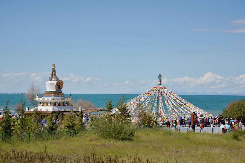 A white stupa with a golden spire, a colorful prayer wheel, and a crowd by the sea. 5