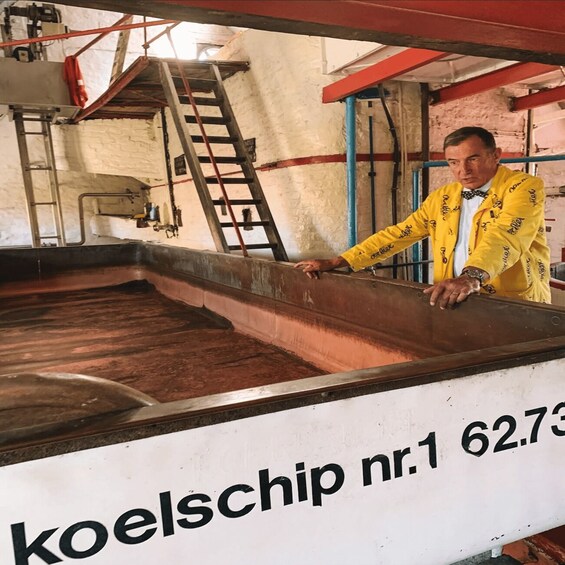 A person in a yellow jacket leaning on a large industrial tank with a sign reading 'koelschip nr.1 62.73'. 1