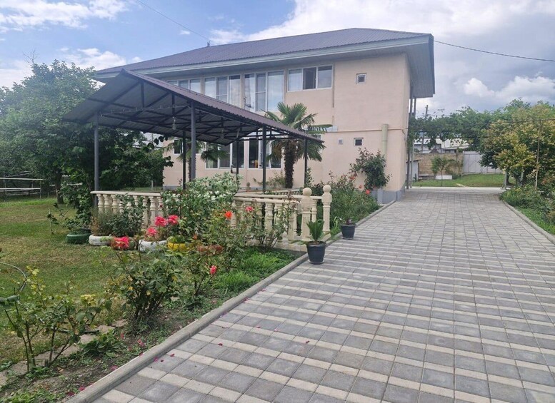 A residential building with a covered porch, a paved driveway, and a garden with flowering plants. 3