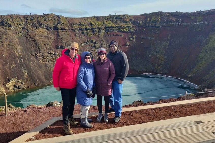 A group of people standing on a viewing platform overlooking a large body of water surrounded by rocky terrain. 2