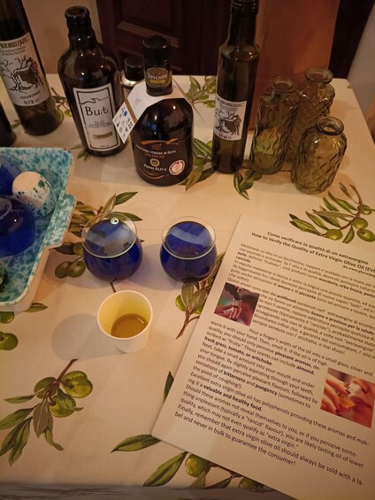 A table with various olive oil bottles, glasses, and a pamphlet. 4