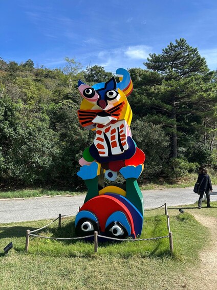 A colorful sculpture of a cat with a leash in a grassy area. 2