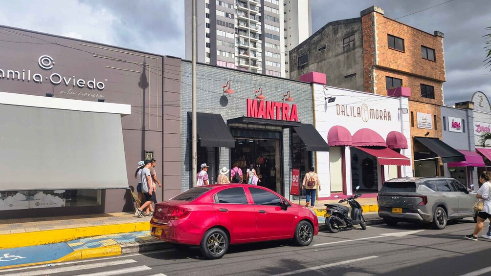 A street with a red car parked on the side, a building with a sign reading 'MANTRA,' and another building with a sign 'DALILA MORAN.' 4
