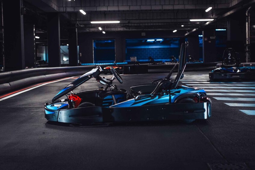 A blue race car with its hood open, parked in a dimly lit indoor racing track. 5