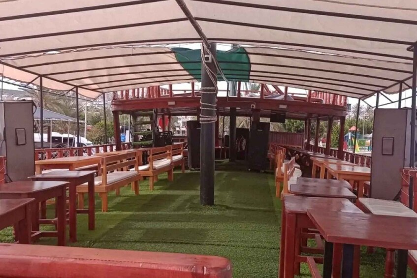 An outdoor seating area with wooden tables and benches under a large canopy. 3