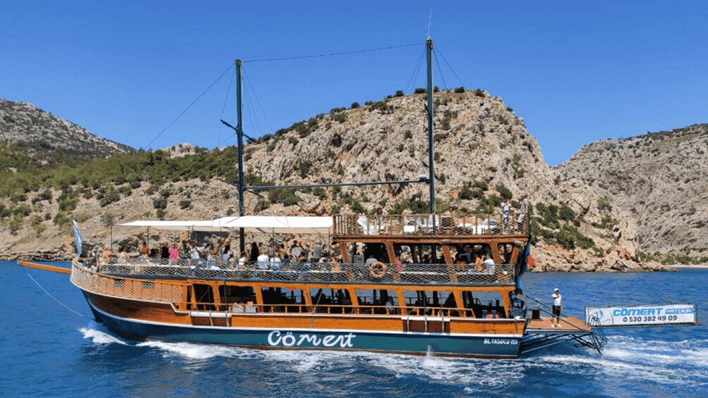 A boat named Comert on a body of water with rocky hills in the background. 1
