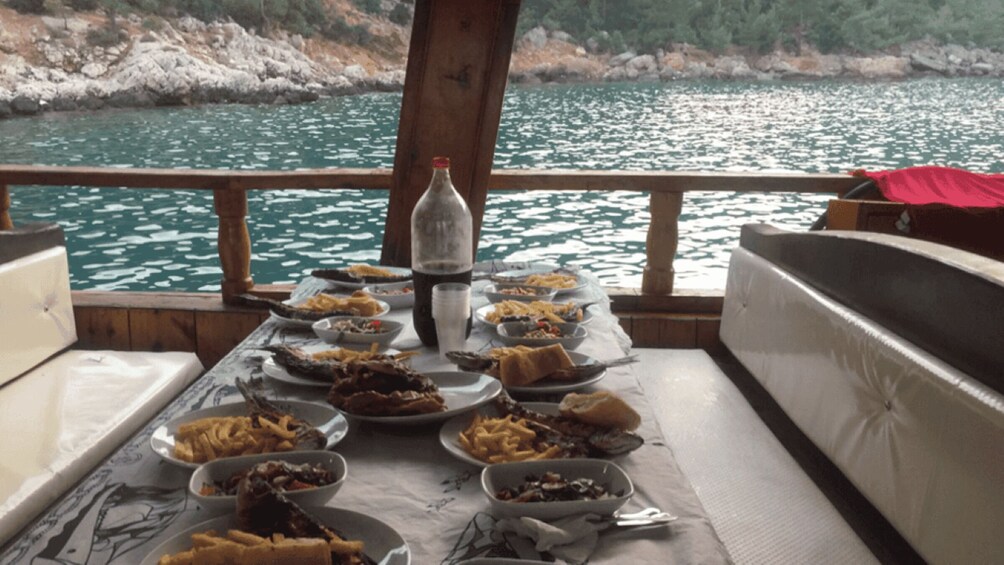 A table with various dishes on a boat, surrounded by water and a rocky shoreline. 5