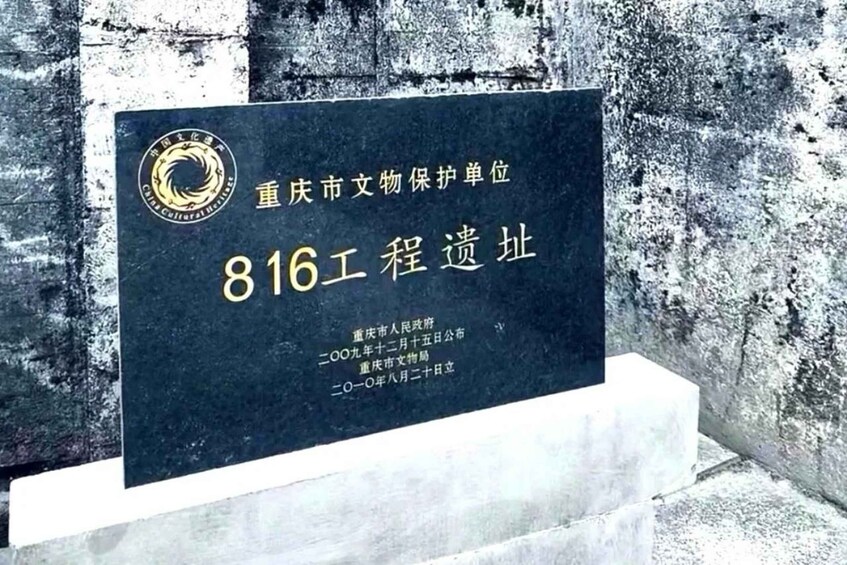 A dark blue plaque with gold lettering on a white pedestal against a textured wall. 4