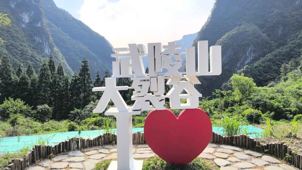 A sign with Chinese characters, a red heart symbol, and a mountainous landscape with a turquoise pool. 2