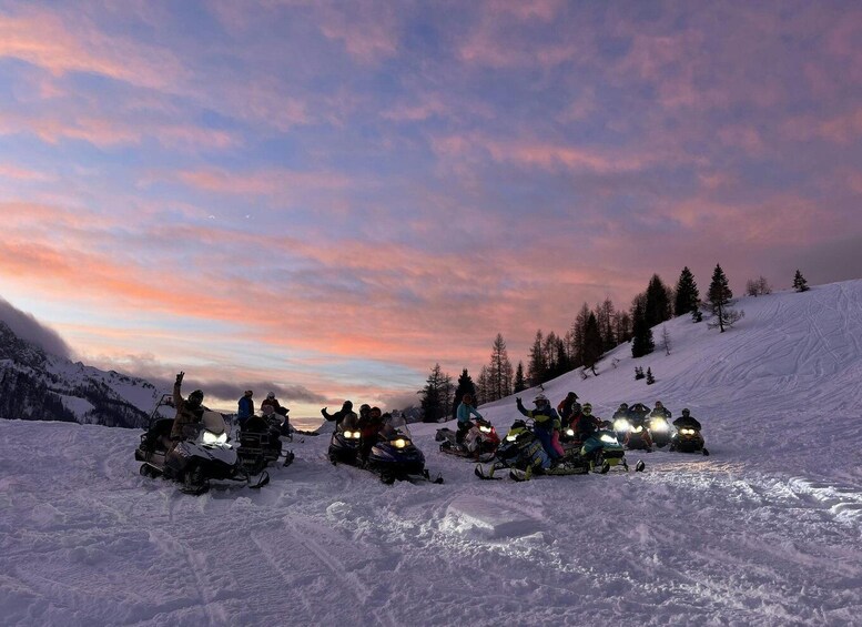 A group of snowmobiles on a snowy slope with a sunset sky. 1