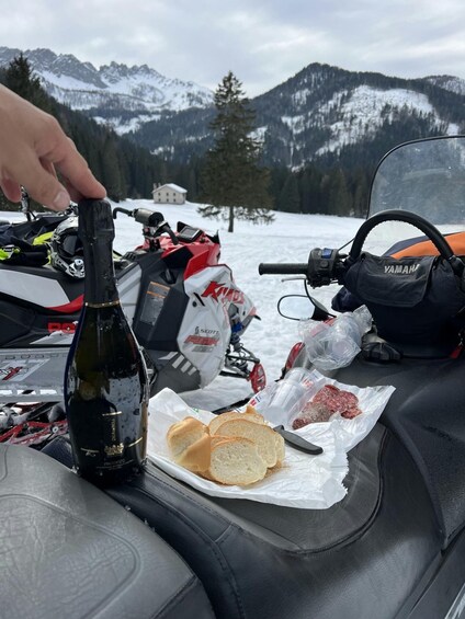 A snowmobile with a bottle of champagne, bread, and meat on the seat. 3