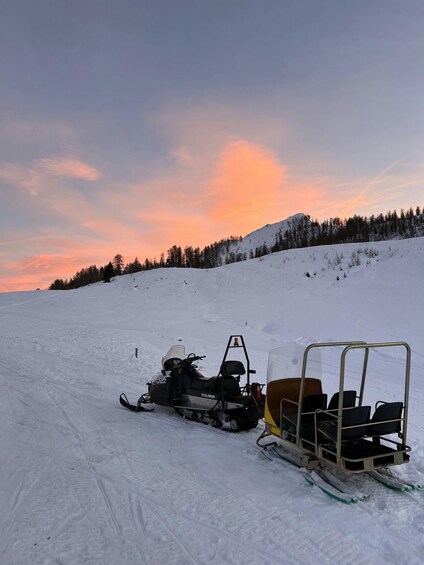 A snowmobile and a sled on a snowy slope with a sunset in the background. 2