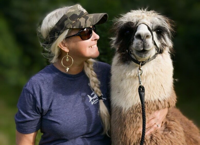 A person wearing a camouflage cap and a blue t-shirt sitting next to a llama. 5