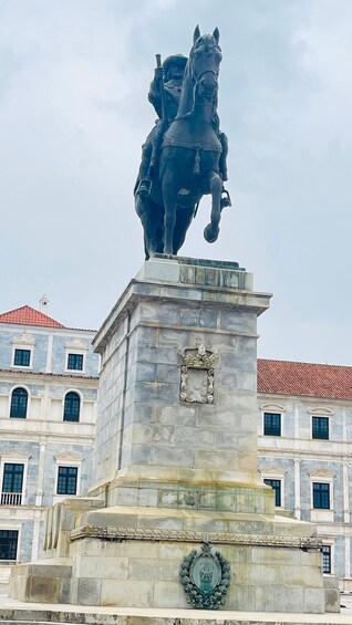 A statue of a man on horseback atop a stone pedestal with a coat of arms, set against a backdrop of classical architecture. 3