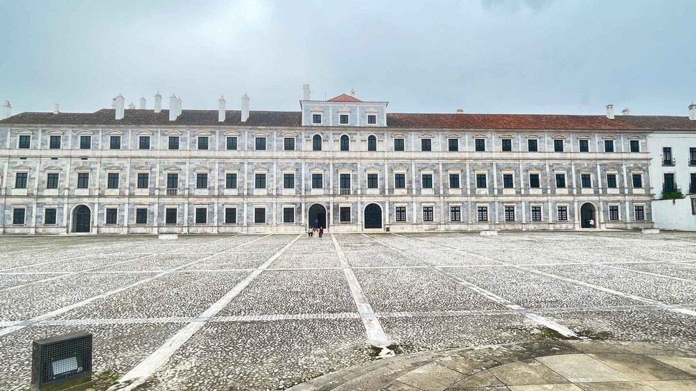 A large historic building with a symmetrical facade, a central courtyard, and a tiled ground. 1
