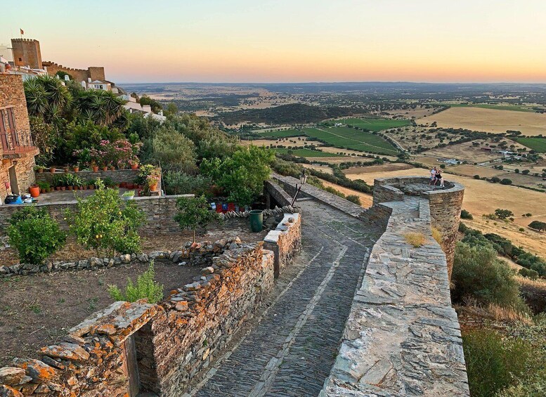 A stone wall with a view of a valley and a castle. 2