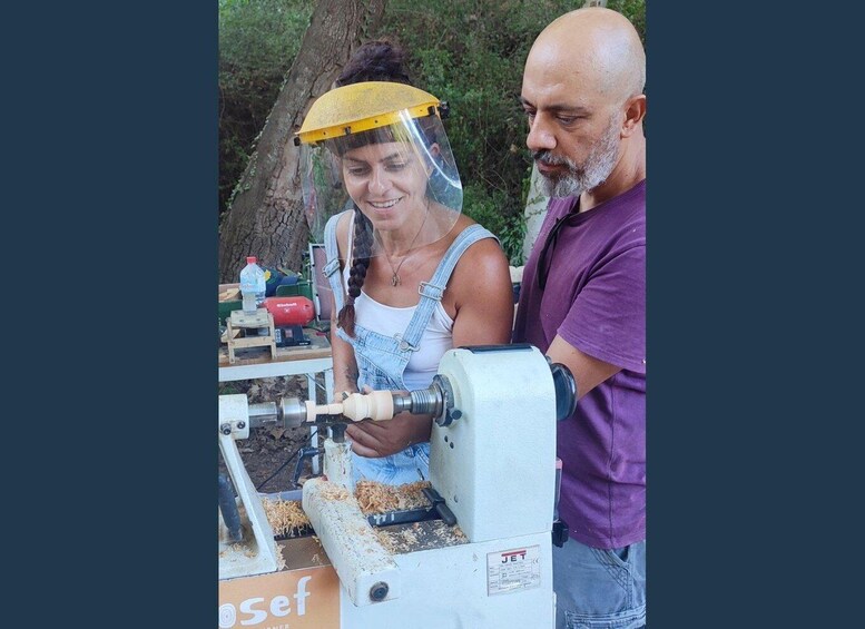 A person operating a woodworking machine outdoors, with a tree and a table with tools in the background. 1