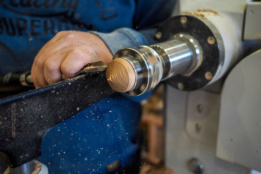 A person using a lathe machine to shape a cylindrical metal object. 3