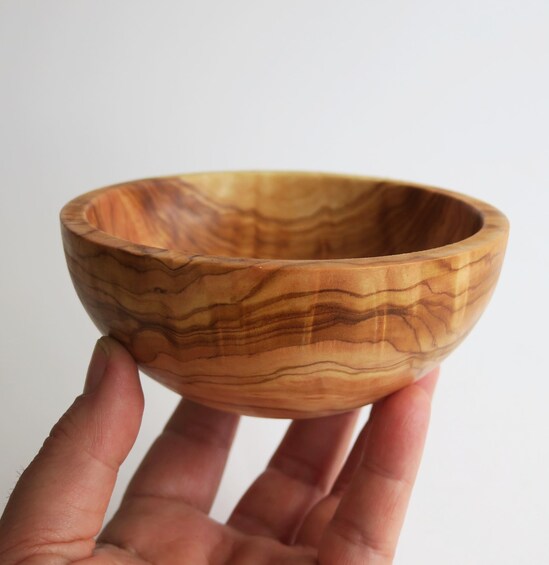A hand holding a wooden bowl with a wavy pattern. 2