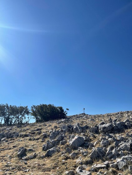 A rocky hillside with sparse vegetation and a cross on top. 5