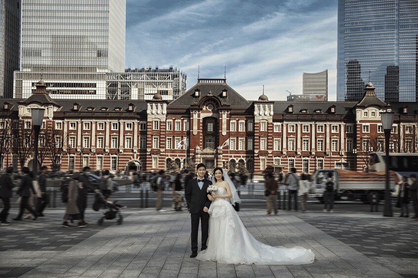 A couple in wedding attire standing in front of a historic building with modern skyscrapers in the background. 2