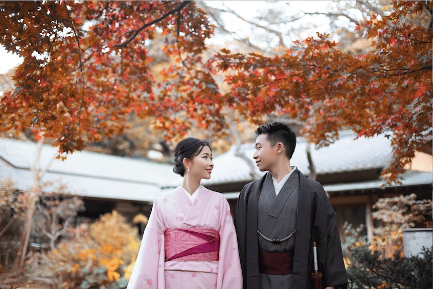 A couple in traditional Japanese attire standing under a tree with autumn leaves. 5
