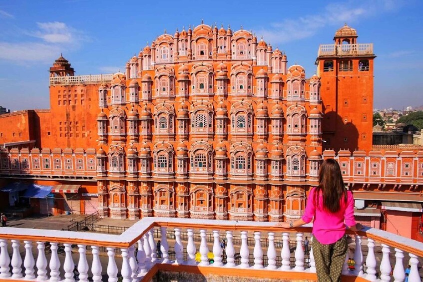 A large, ornate building with multiple domes and arches, a balcony with white balustrades, and a clear blue sky in the background. 3