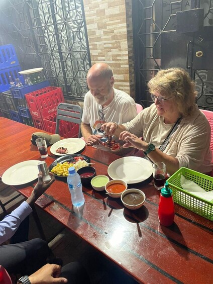 Two people dining at a table with various dishes, including a plate of fries, a bowl of soup, and a bottle of water. 1