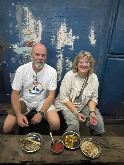 Two people sitting on a bench with food in front of them. 5