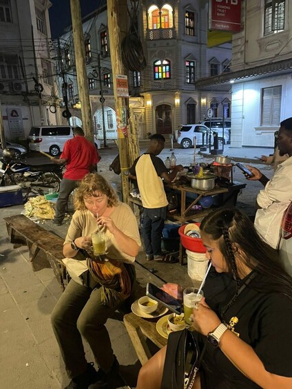 People sitting on benches outdoors at night, with buildings and a street in the background. 4