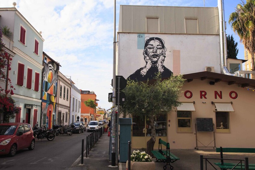 A street with parked cars, a mural on a building, and a restaurant named 'ORNO'. 1