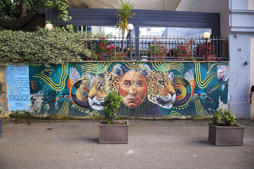 A mural with colorful wildlife and text on a wall, surrounded by potted plants and a metal fence. 3