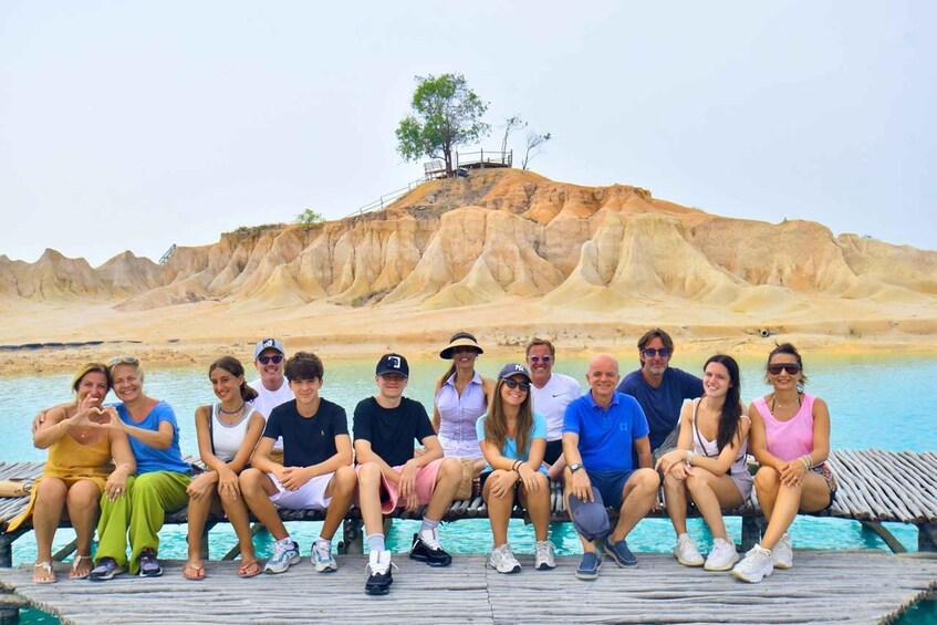 A group of people sitting on a wooden dock by a body of water with a unique geological landscape in the background. 1