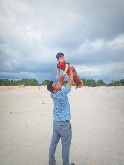 A man lifting a child in an open, sandy area with sparse vegetation and a cloudy sky. 4