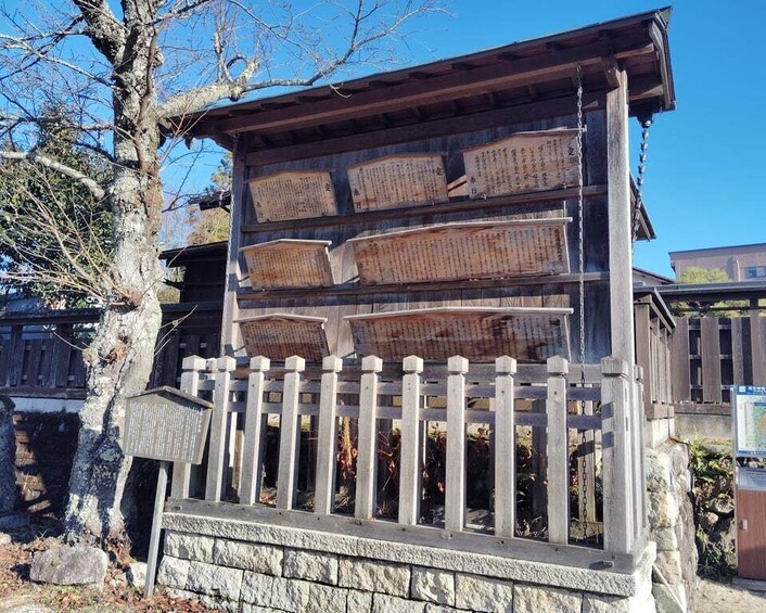 A wooden structure with multiple boards displaying text, a stone wall, and a wooden fence. 5