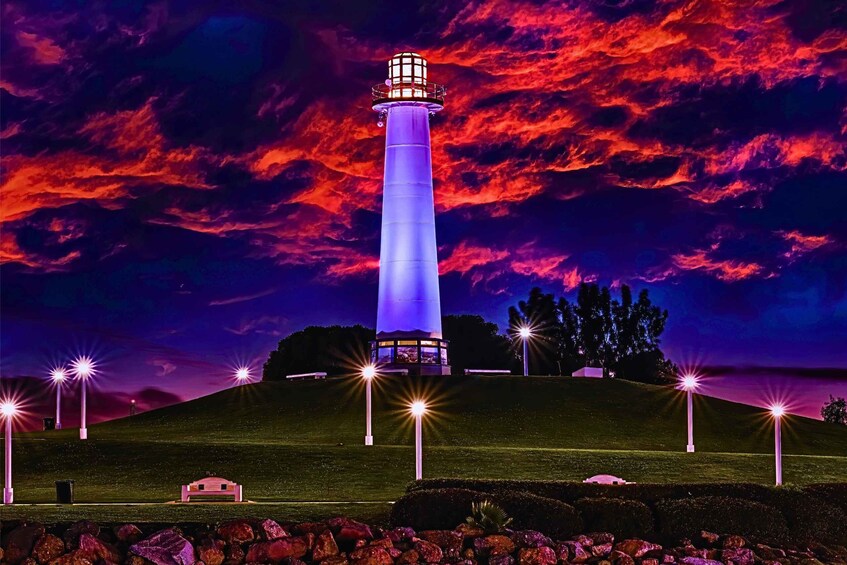 A lighthouse with a blue light on a hill, surrounded by trees and a sunset sky. 2