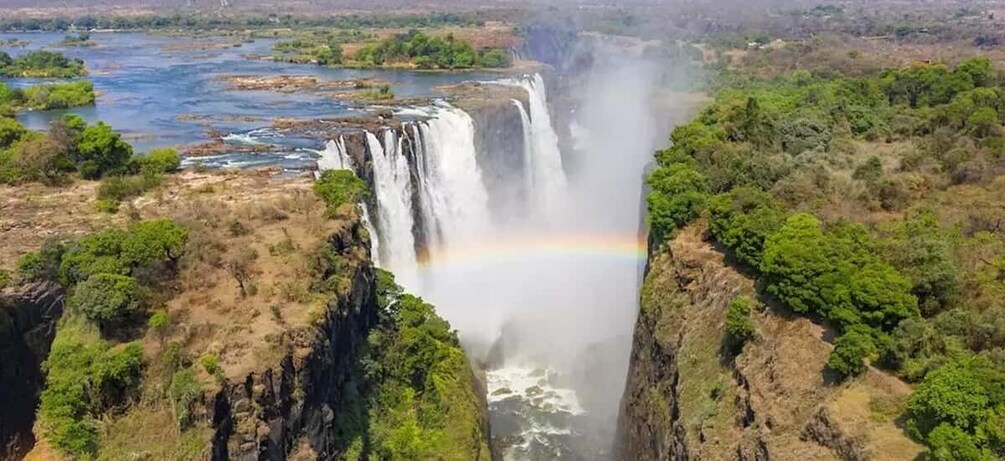 A waterfall with a rainbow, surrounded by greenery and a river. 2