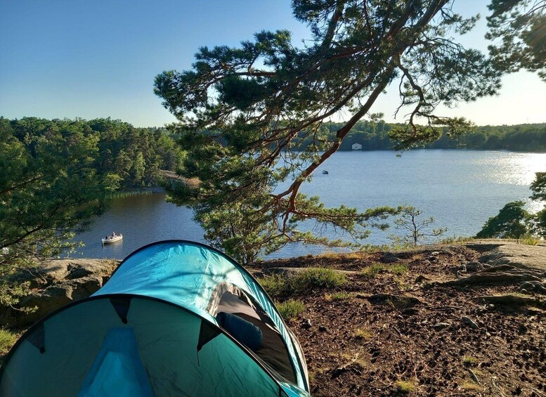 A tent set up on a rocky shore overlooking a lake with trees and a boat in the distance. 5