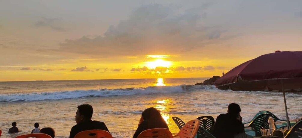A sunset over the ocean with people sitting on chairs facing the water. 4