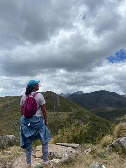 A person hiking on a mountain trail with a backpack, surrounded by green hills and a cloudy sky. 1