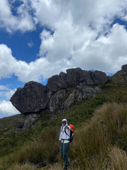 A hiker on a grassy hill with a rocky outcrop in the background. 5