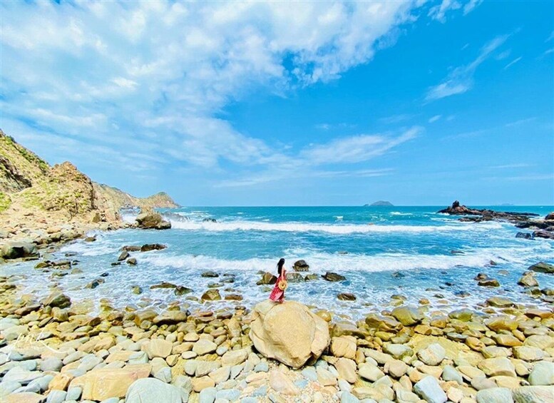 A rocky beach with waves, a clear sky, and a person standing on a rock. 3