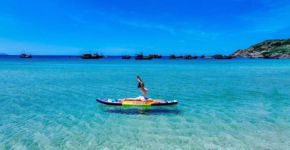 A person on a colorful raft in clear blue water with several boats in the background. 1