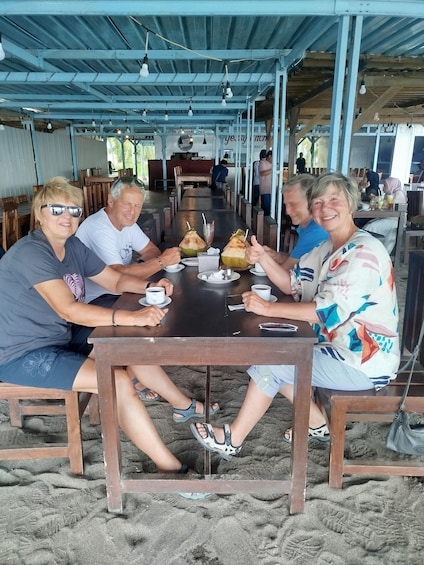 A group of people sitting at a wooden table under a blue roof, with drinks and a menu in front of them. 1